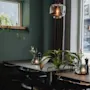 A cozy dining area at Home Hotel Uppsala with dark green walls, tables set with plants and candles, and a window showing a street with PONG.