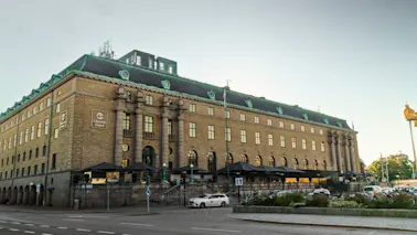 Clarion Hotel Postin ulkokuva, upea rakennus vihreällä katolla ja ulkoruokailualueilla, kadun vieressä.