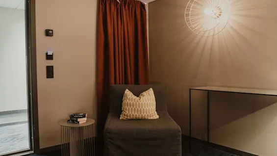 Viihtyisä nurkkaus, jossa on mukava tuoli, sivupöytä kirjoineen ja lämmin valaisin, mikä viittaa rauhalliseen lukupaikkaan.