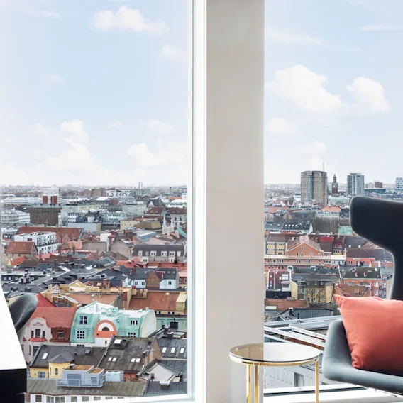 A comfortable room with a large window offering a panoramic view of a vibrant city with diverse architecture.