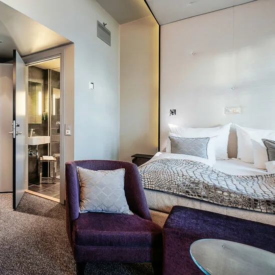 Et moderne hotellrom med luksuriøse møbler, en stor seng, og en åpen dør som fører til et annet rom.