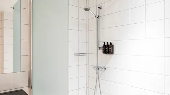 A clean, modern shower area with white tiled walls, a shower head, and wall-mounted toiletries, ready for use.