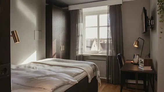 Ett mysigt hotellrum på Home Hotel Grand, Helsingborg, med en bekväm säng, en skrivbordshörna och naturligt ljus från fönstret.