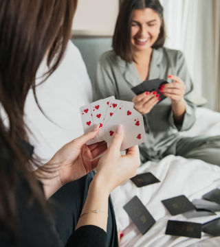 Two friends playing a game of cards in the hotel bed.