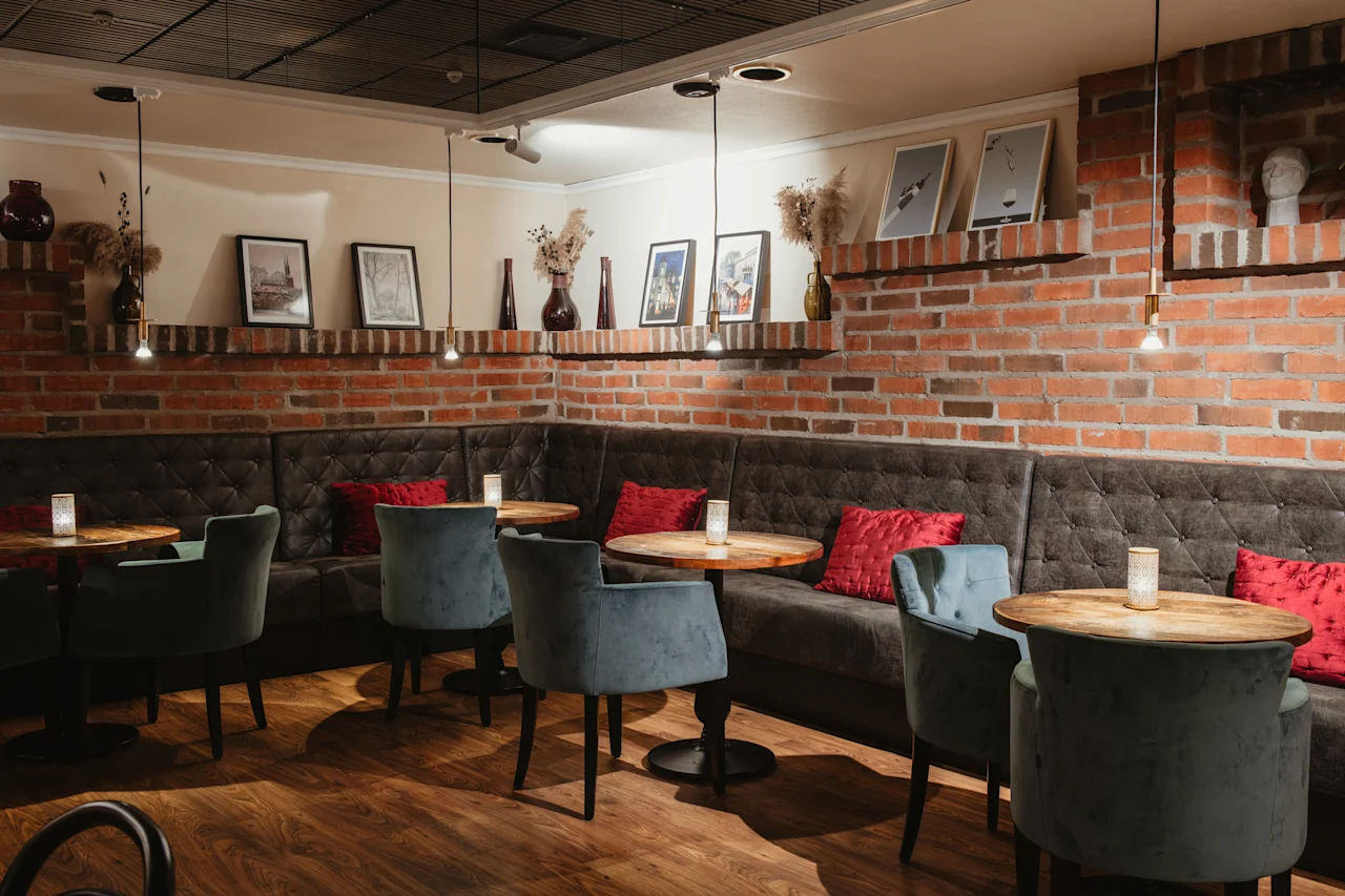 En mysig lounge med mörkgrå bänksoffor, ljusblå stolar och små träbord med levande ljus. Exponerade tegelväggar är dekorerade med konst.