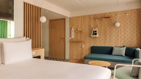 A modern and cozy hobo oslo hotel room with a bed, a green sofa, and a unique pegboard wall with a HO BO bag.