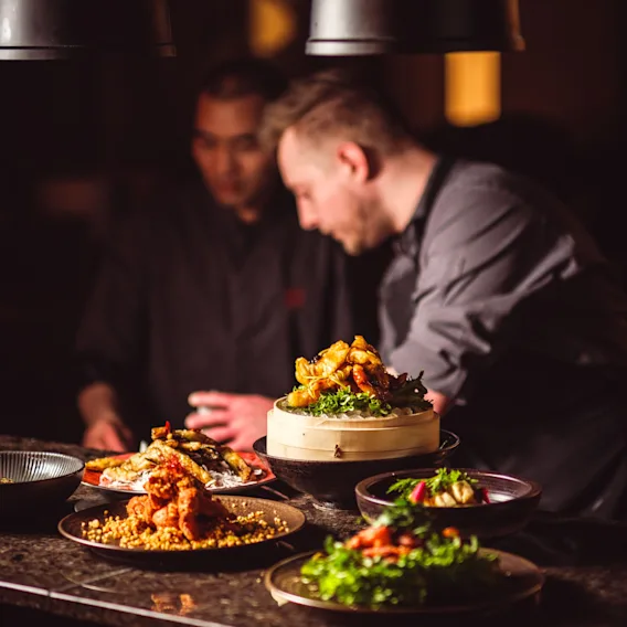 Two chefs preparing and plating delicious-looking food in a restaurant kitchen.