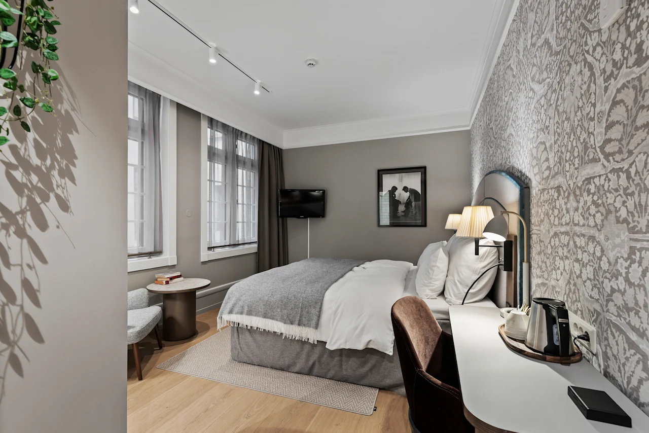 A stylish hotel room with a large bed, a functional workspace, and a relaxing corner, designed for comfort and productivity.