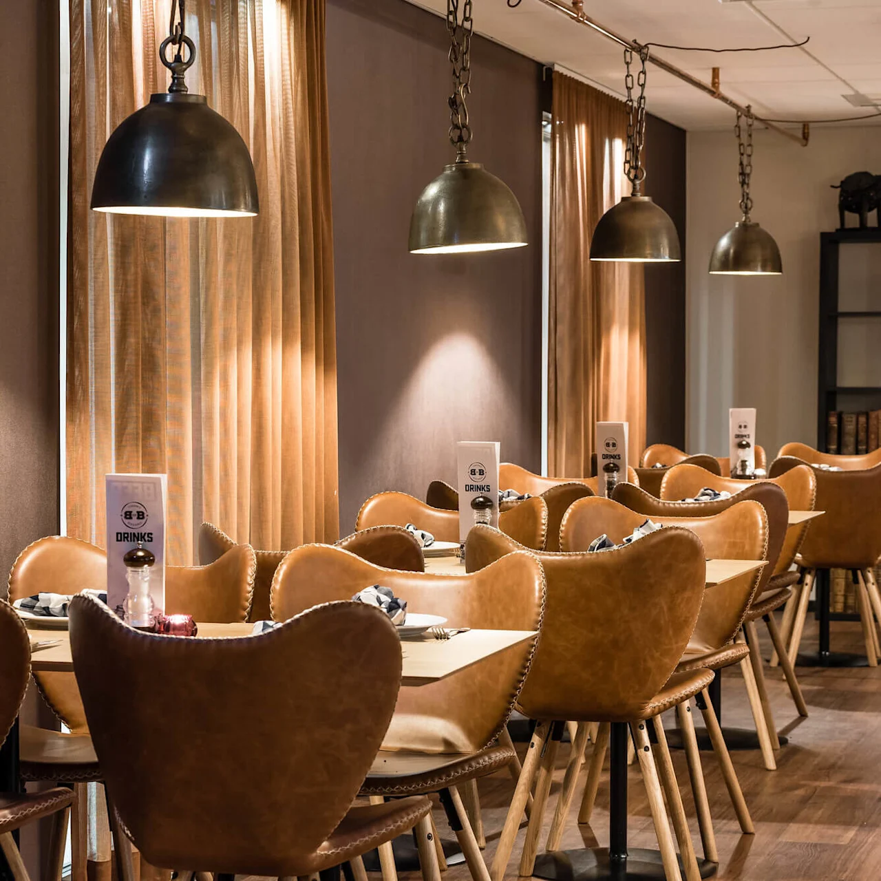 En mysig restauranginteriör med hänglampor som lyser upp en rad läderstolar vid träbord.