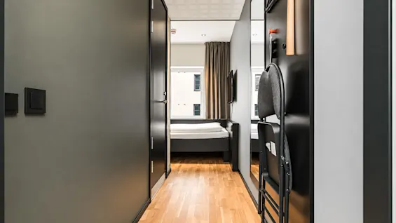 Modern hotel room hallway with wooden floors leading to a bed by the window.