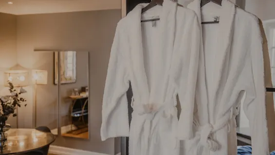 Två mjuka vita badrockar hänger i ett mysigt hotellrum på Home Hotel Grand, Helsingborg, inbjudande till avkoppling.