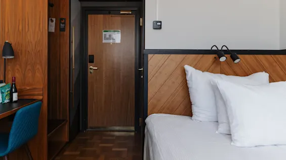 Ett hotellrums interiör med träelement, en enkelsäng och en entrédörr.