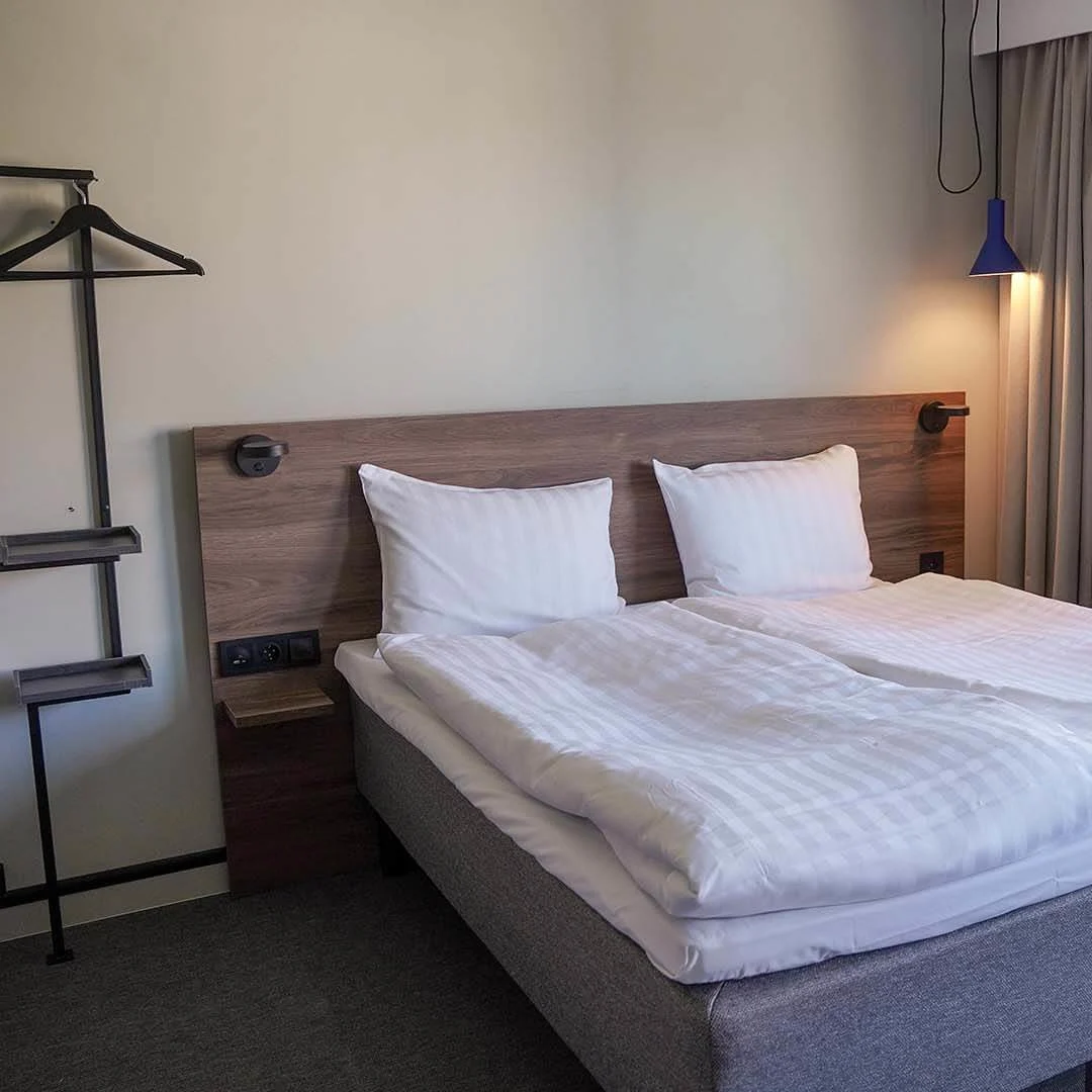 A tidy double bed in a room with a window, modern furnishings, and soft lighting.