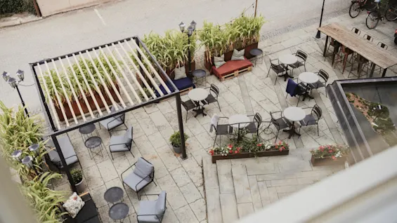 An inviting outdoor patio at Home Hotel Uppsala with various seating areas, lush greenery, and a pergola, perfect for relaxation.