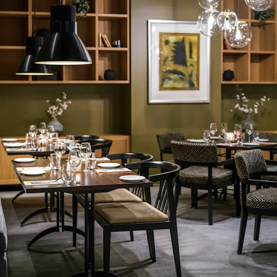 Bordene er dekket med glass og tallerkener i en moderne restaurant, omgitt av stilige stoler og myk belysning fra hengende lamper, og skaper en elegant spiseopplevelse.