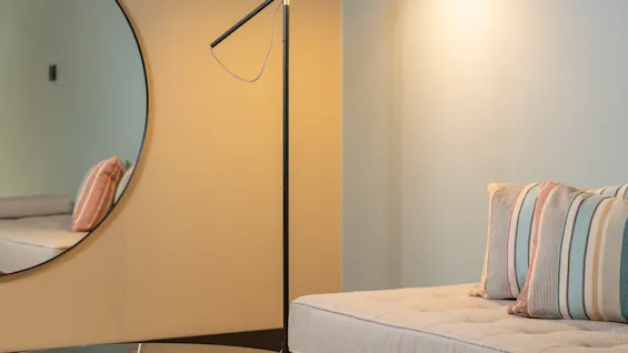 En mysig hörna med en modern golvlampa som lyser upp en dagbädd med randiga kuddar, ett runt soffbord och en stor spegel.