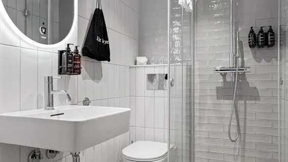 Home Hotel Gabelshus: Et lyst, moderne bad med vask, toalett og glassdusj. En pose merket hårføner henger i nærheten.