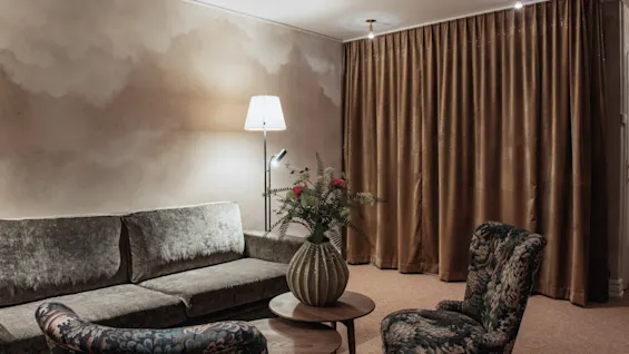 Home Hotel Baltzar - Family Room. A warm and inviting living area with a comfortable sofa, patterned armchair, and floral decor.