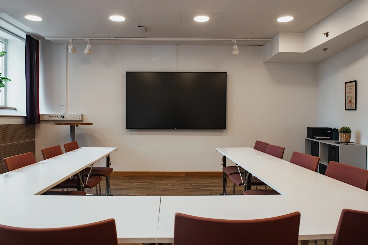 A modern meeting room at Home Hotel Uppsala with a large screen, U-shaped table, and chairs, ready for presentations.
