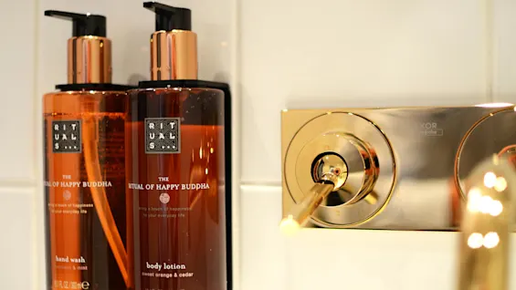 Two amber-colored bottles labeled "RITUALS", one a hand wash and the other a body lotion, beside a gold-toned bathroom faucet.