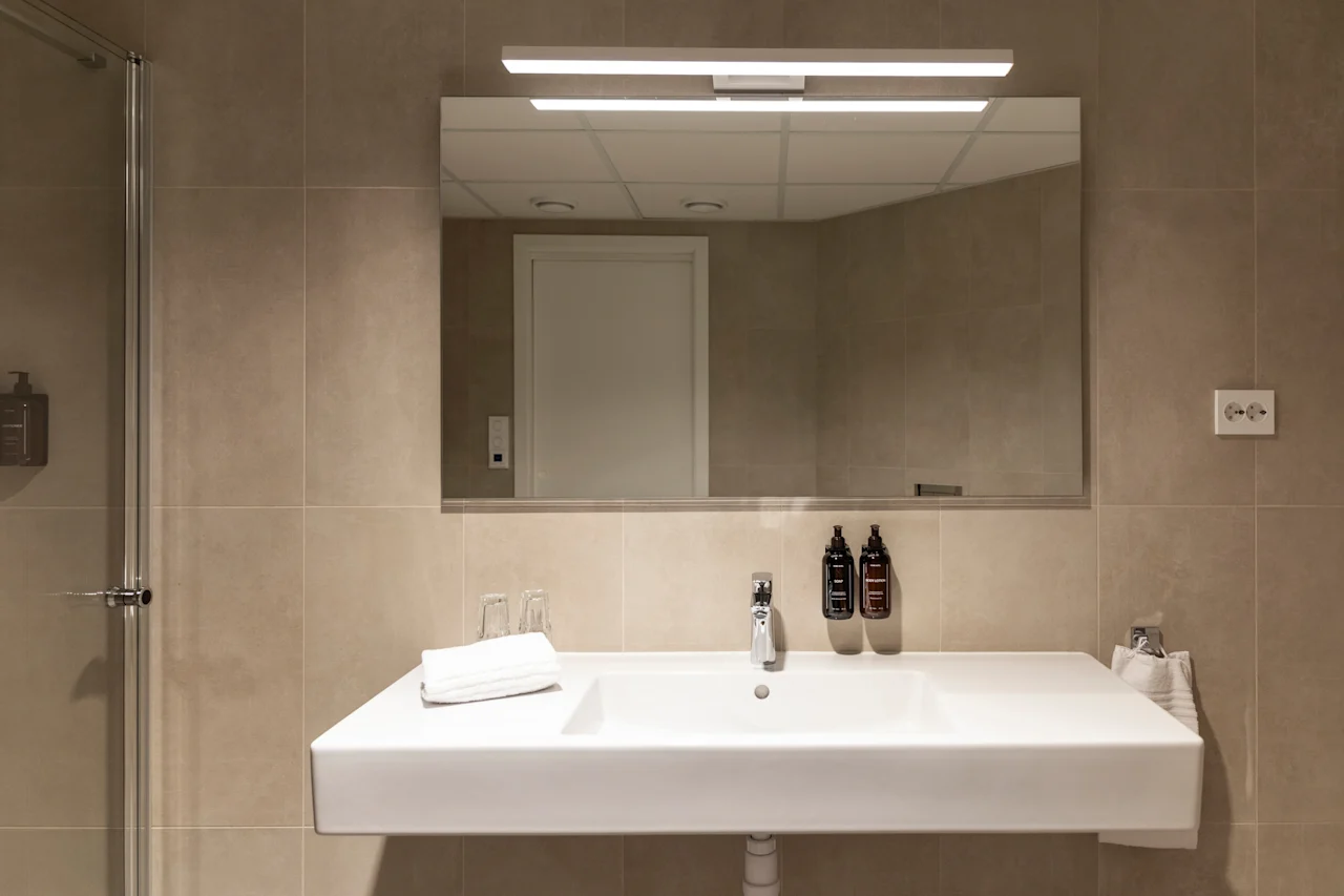 A clean, modern bathroom sink area with a large mirror, toiletries, and fresh towels, ready for use.
