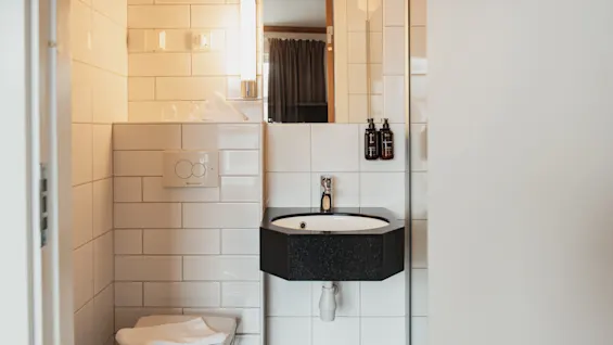 A clean, modern bathroom with white tiled walls, a black sink, and a toilet with a fresh towel.