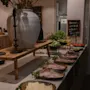 Buffébord med olika köttpålägg, grönsaker och örter. Stor vas och ljushållare pryder uppsättningen. En griffeltavla i bakgrunden lyder: "Gør morgen maden der hjemme værd at stå op for."