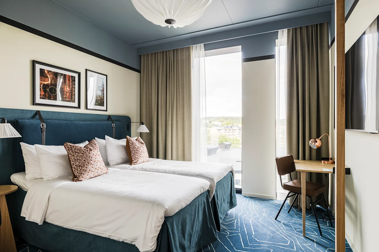 Et moderne hotelværelse på Hernö Gin Hotel med to komfortable senge, et skrivebord og et stort vindue med udsigt.