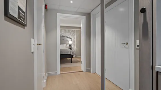 A hotel hallway with a framed sign that reads "Welcome to our hotel" leading to a cozy bedroom.