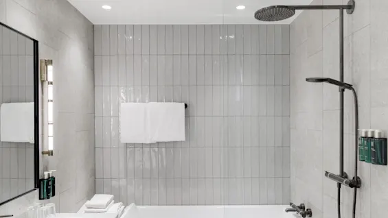 A modern bathroom with a white bathtub, rain showerhead, glass partition, and tiled walls in neutral tones.