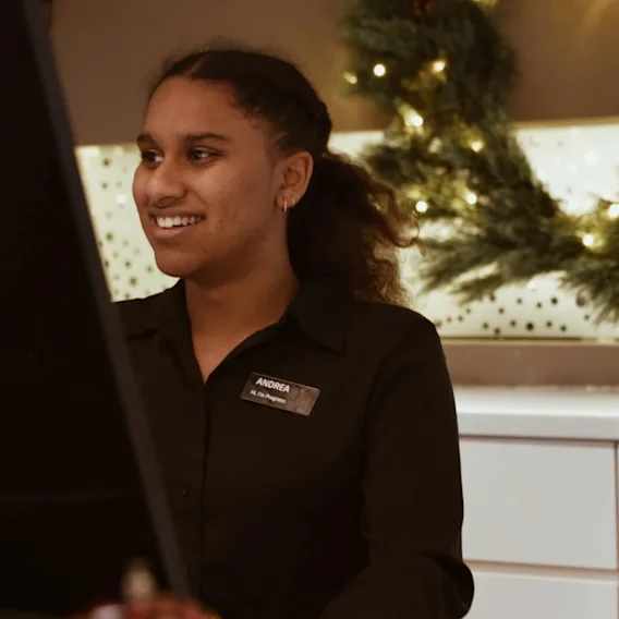 En smilende person i svart uniform ser på en skjerm, med festlige dekorasjoner i bakgrunnen.