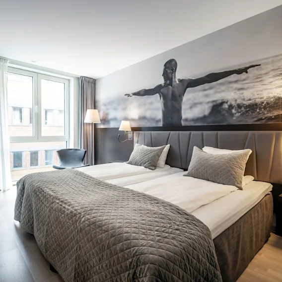 A cozy hotel room at Quality Hotel Waterfront in Ålesund featuring a large wall mural of a man balancing.
