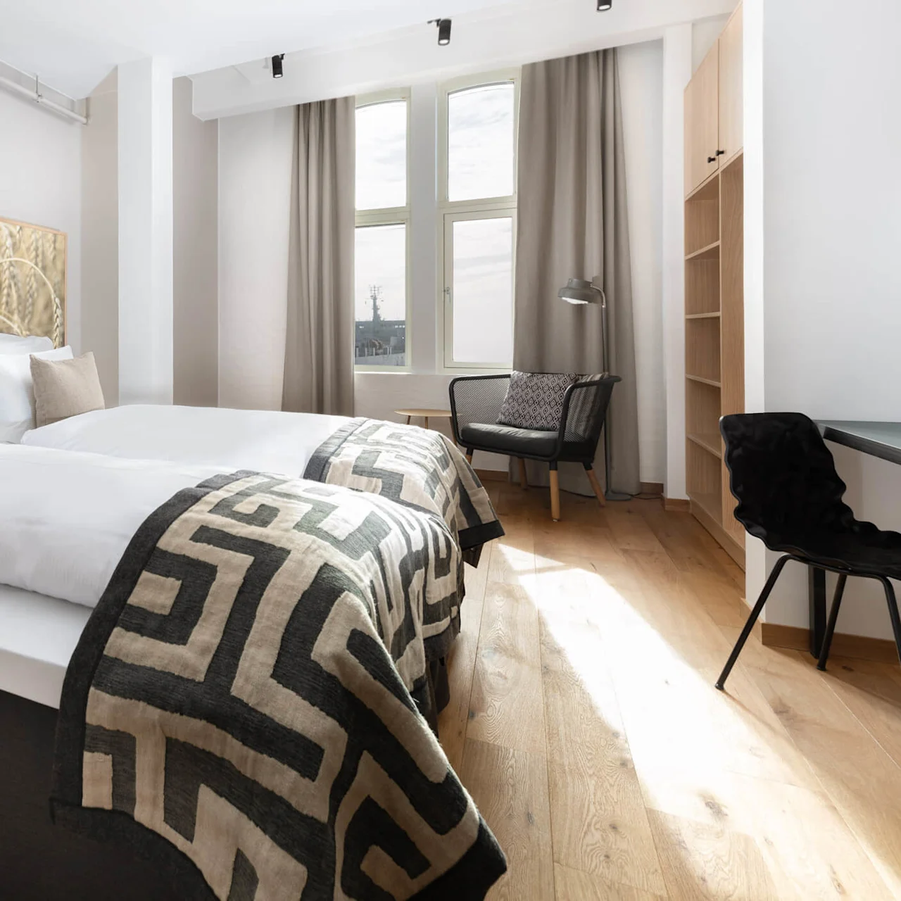 A neatly made bed with patterned throw blankets in a room with modern furnishings and a large window, exuding a cozy atmosphere.