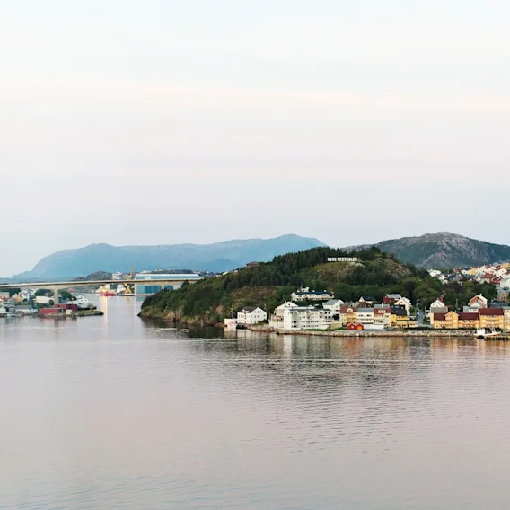 Malerisk kystutsikt over Kristiansund med fargerike hus ved sjøen, blikkstille vann, en bro og grønne koller.