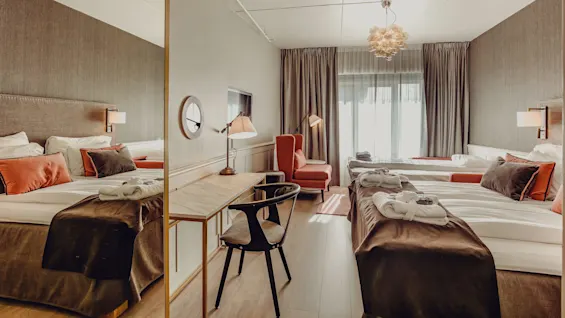 Two neatly arranged beds with plush headboards in a well-lit, stylish hotel room with contemporary decor.
