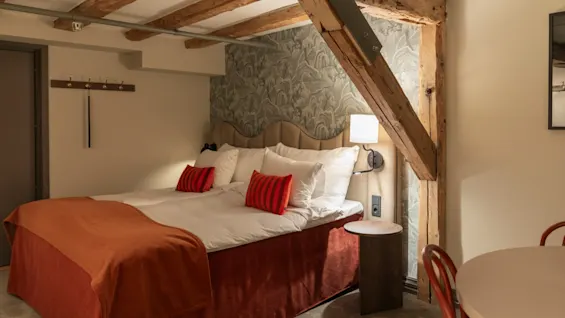 Et koselig hotellrom med en stor seng, synlige trebjelker og et lite spiseområde, som antyder et komfortabelt opphold.