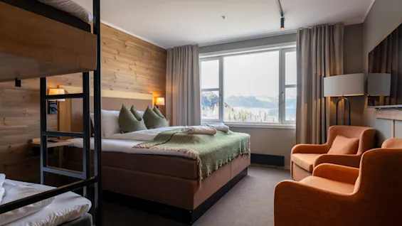 Ett mysigt hotellrum med en stor säng, våningssängar och två fåtöljer, med en naturskön utsikt över ett snöigt landskap.