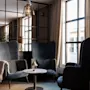 A comfortable lounge space featuring plush armchairs, a small table, and a bright window, with a person working nearby.