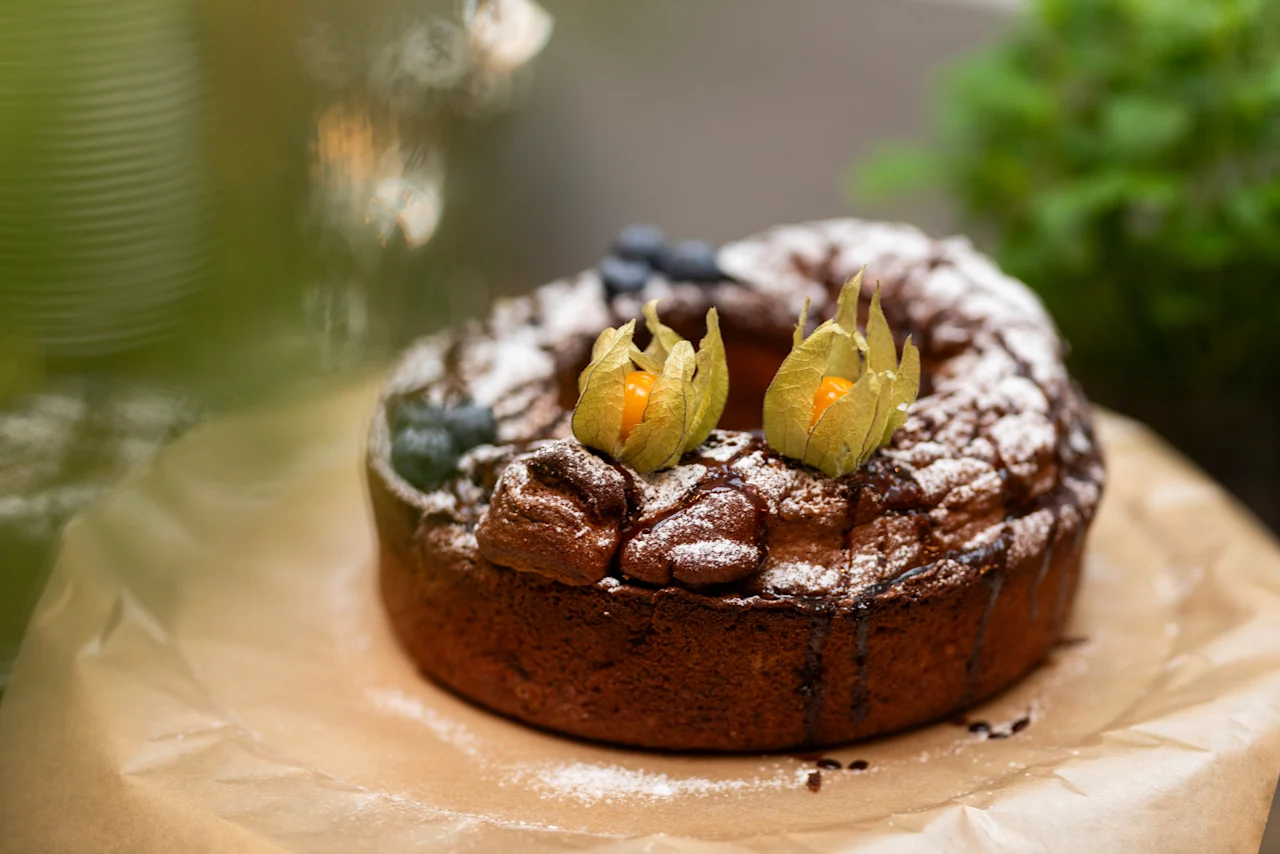A delicious bundt cake dusted with powdered sugar, drizzled with chocolate, and garnished with physalis and blueberries. Home Hotel Grand Bodø.