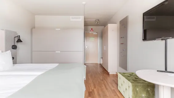 A bright and modern hotel room with twin beds, a TV, and a comfortable seating area.