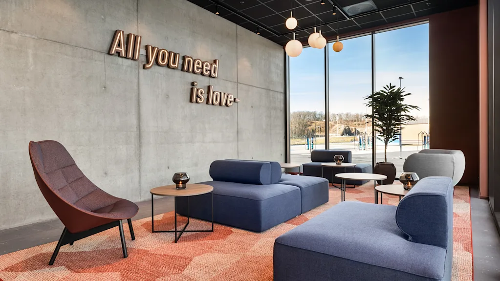 Et moderne og innbydende loungeområde med blå sofaer, mønstret teppe og betongvegg med teksten 'All you need is love'.