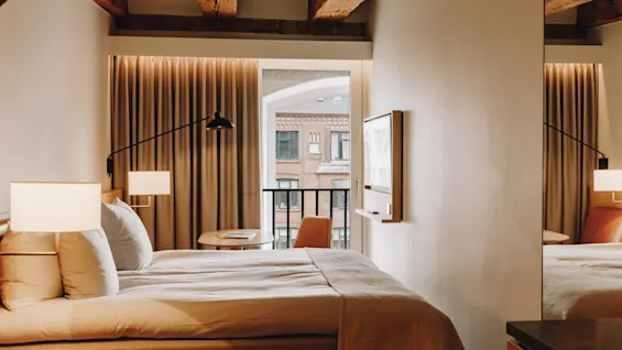 Ett mysigt hotellrum med en bekväm säng, varm belysning och en balkong med utsikt över en stadsgata.