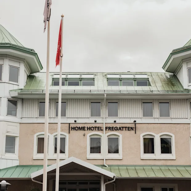 Udvendig udsigt over en hotelbygning med grønne tage og karnapper. Et skilt på facaden læser HOME HOTEL FREGATTEN.