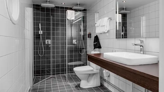 A modern bathroom interior with a shower, toilet, and sink against tiled walls, showcasing cleanliness and functionality.