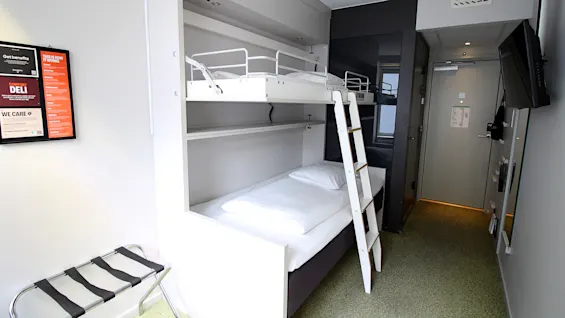 Moderni hotellihuone, jossa on valkoinen kerrossänky ja tikkaat.