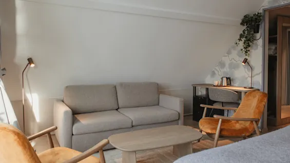 Et komfortabelt og veloplyst hotelværelse med et siddeområde og en dedikeret arbejdsplads, perfekt til afslapning eller produktivitet.