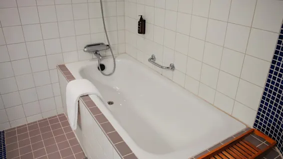 A clean and inviting bathroom at Home Hotel Uppsala, featuring a bathtub with a shower, a fresh towel, and a wooden bath caddy.