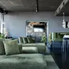 Grønne sofaer står i en elegant, moderne lounge med mørke vegger og gulv. Hengende pendellamper lyser opp rommet, med potteplanter og et speil som skaper en stilfull, avslappet atmosfære.