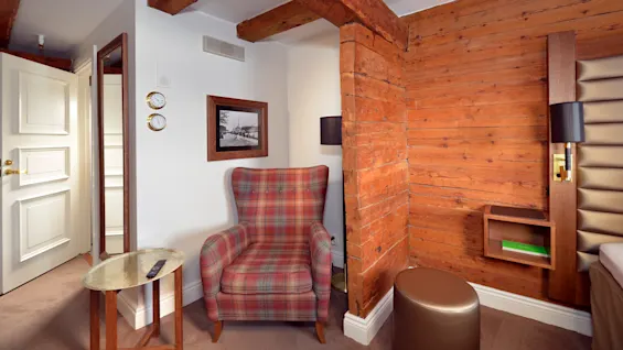A plush, checkered armchair sits in a cozy, rustic room with exposed brick walls and wooden beams.