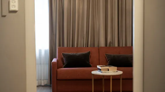 Ett mysigt och inbjudande hotellrum med en bekväm soffa, ett litet bord med böcker och mjuka gardiner.